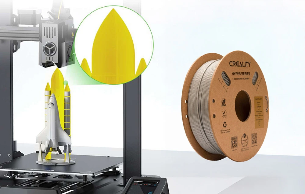 O rachetă galbenă și albă imprimată pe o imprimantă 3D lângă o bobină de filament gri