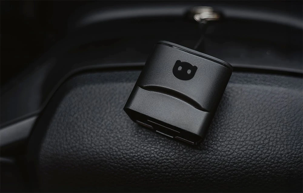 Adaptor de diagnosticare Carly OBD2 negru așezat pe bordul din piele al mașinii