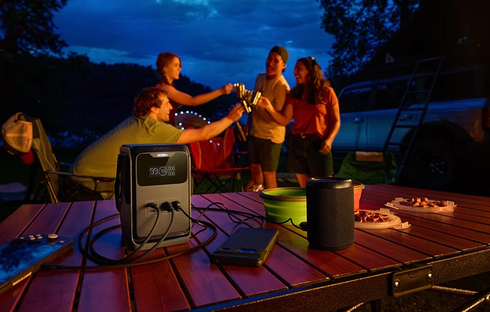 O stație de alimentare pe o masă de camping lângă un difuzor și dispozitive electronice seara