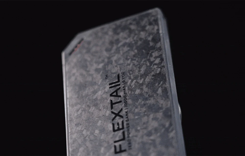 Prim-plan al unei baterii externe subțiri, cu carcasă gri, texturată și logo-ul FLEXTAIL.