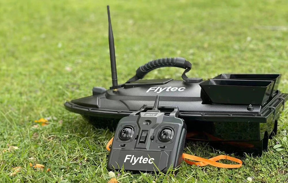 Barca de momeală Flytec neagră cu telecomandă așezată pe iarbă verde