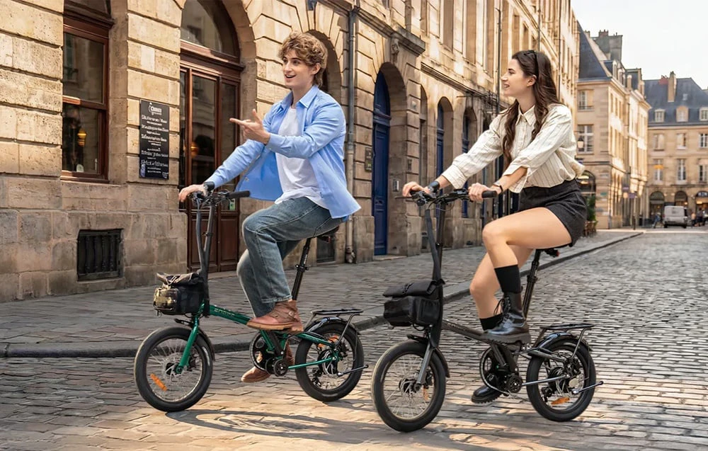 O femeie și un bărbat merg pe biciclete electrice pliabile pe o stradă pietruită din centrul vechi