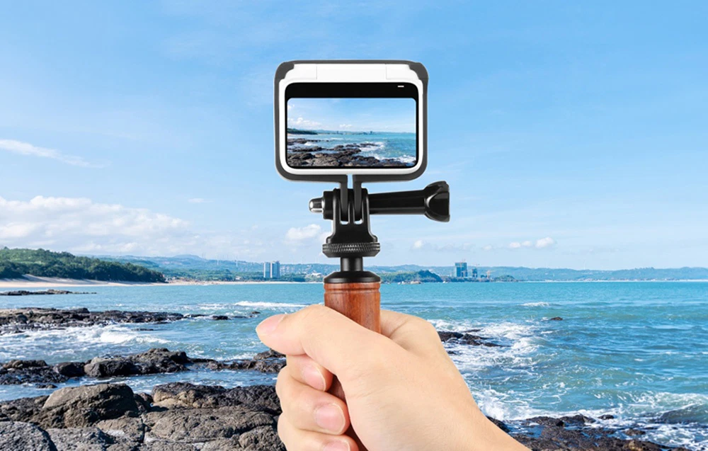 Camera Insta360 GO 3 într-un cadru de montare atașat la un mâner portabil din lemn, lângă mare