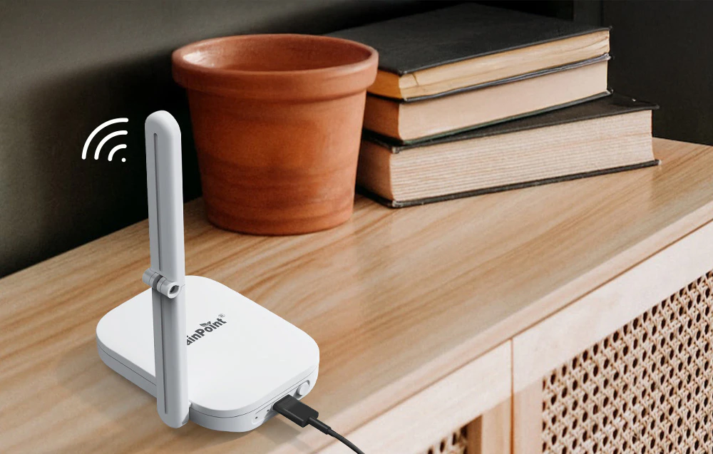 Stația de bază, conectată la un cablu USB cu antena ridicată, se află pe o masă lângă un ghiveci de lut și cărți