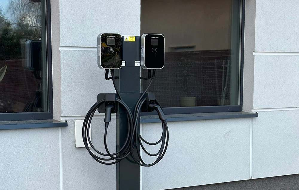 O stație dublă de încărcare a vehiculelor electrice montată pe un stâlp independent în fața clădirii.