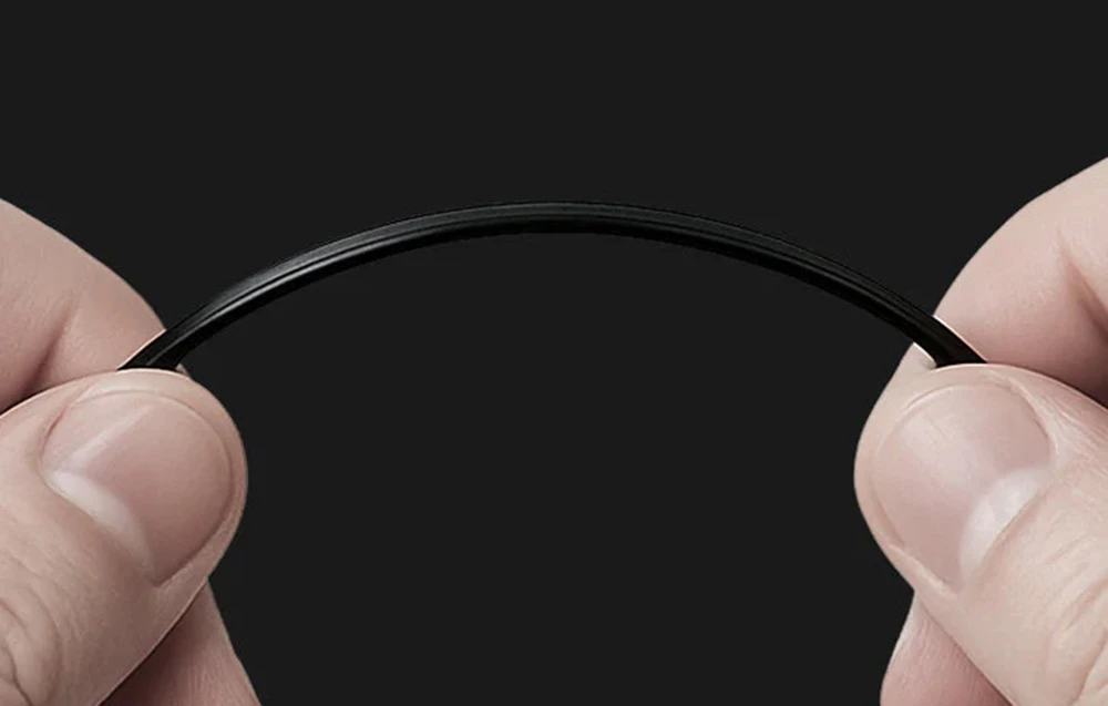 Două mâini țin și îndoaie un filament subțire și negru de imprimantă 3D formând un arc pe un fundal întunecat