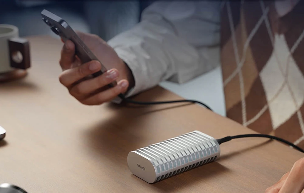 Carcasa pentru unitatea SSD TerraMaster așezată pe un birou din lemn și conectată printr-un cablu la un utilizator care ține un smartphone în mână.