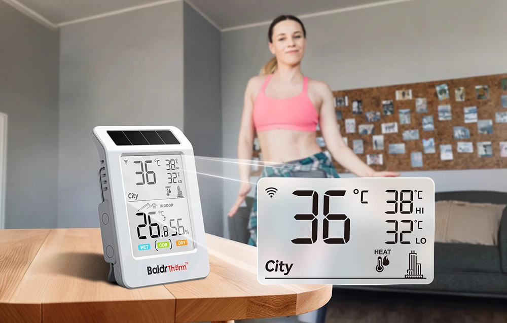 Un termohigrometru BALDRTHERM pe o masă din lemn; în fundal, o femeie dansează în sufragerie, îmbrăcată în ținută sport