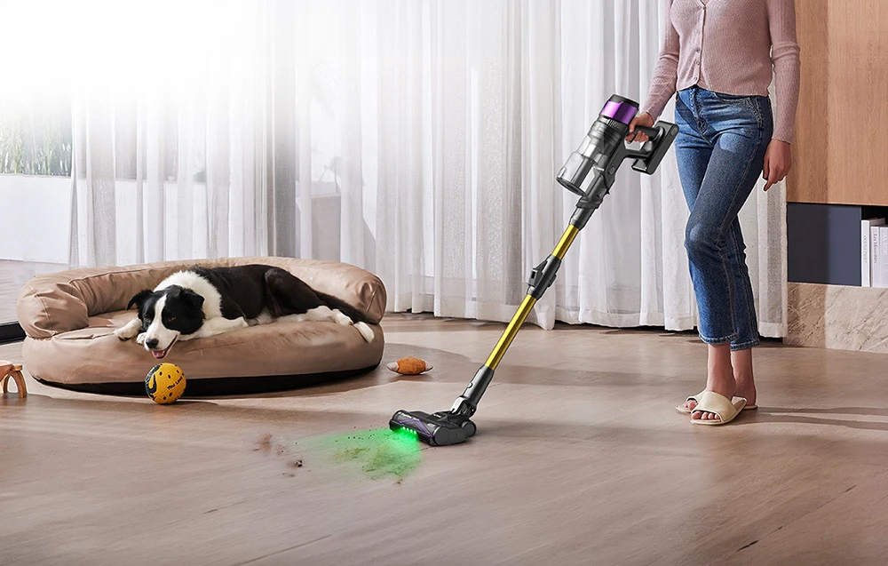 O femeie aspiră podeaua cu un aspirator vertical Ultenic lângă un pat pentru câini, unde doarme un câine