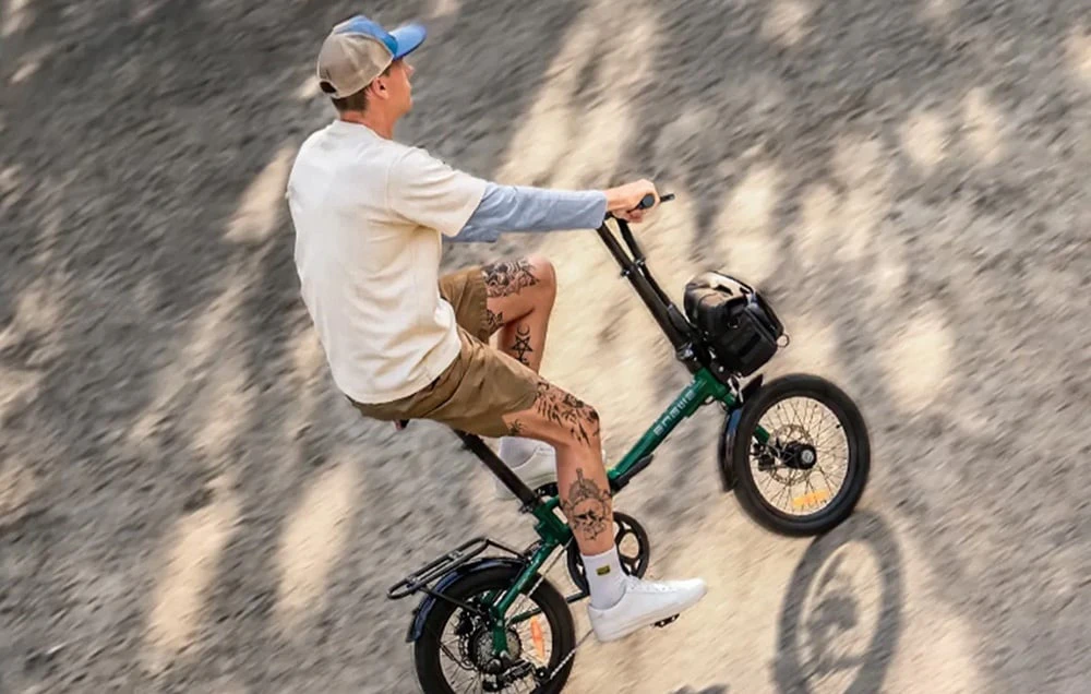 Un bărbat merge cu o bicicletă electrică pliabilă verde pe o suprafață de culoare deschisă