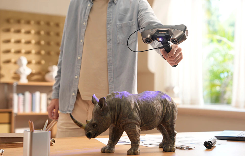 Un bărbat scanează o figurină de rinocer cu un scaner 3D care emite lumină albastră