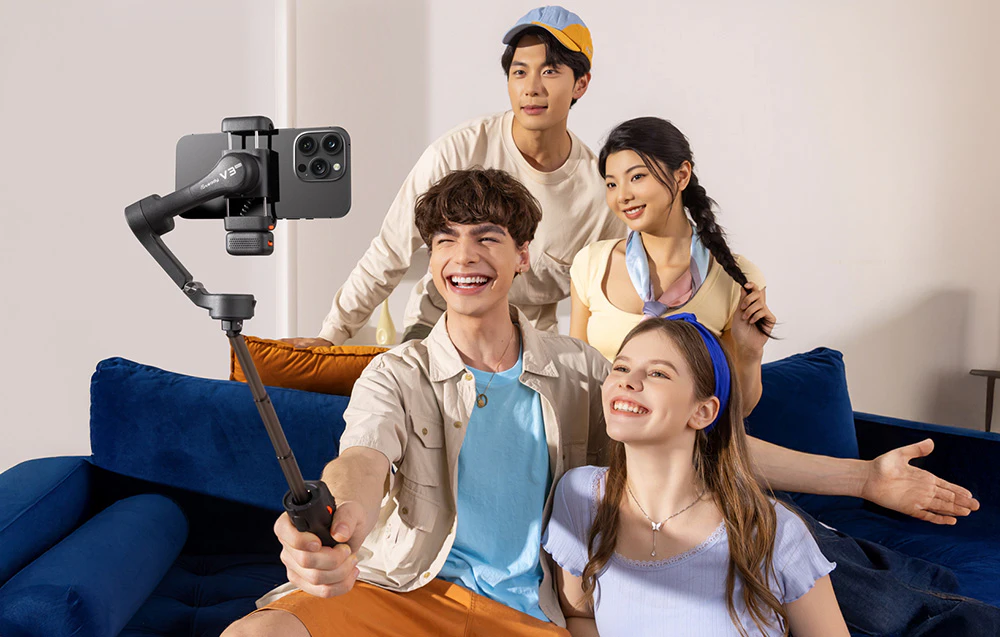 Un grup de patru tineri care își fac un selfie folosind un smartphone montat pe un cardan negru.