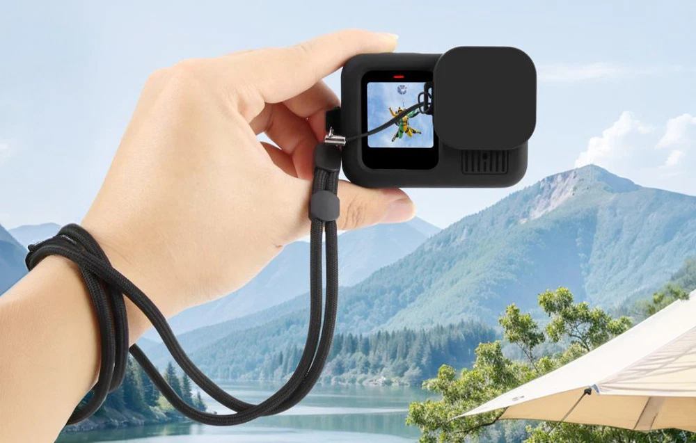 Cameră de acțiune într-o carcasă de protecție din silicon negru cu curea de mână, produs ținut în mână pe fundalul unui peisaj montan.