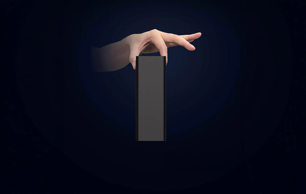 O mână ține o carcasă subțire neagră pentru hard disk, poziționată vertical pe un fundal întunecat