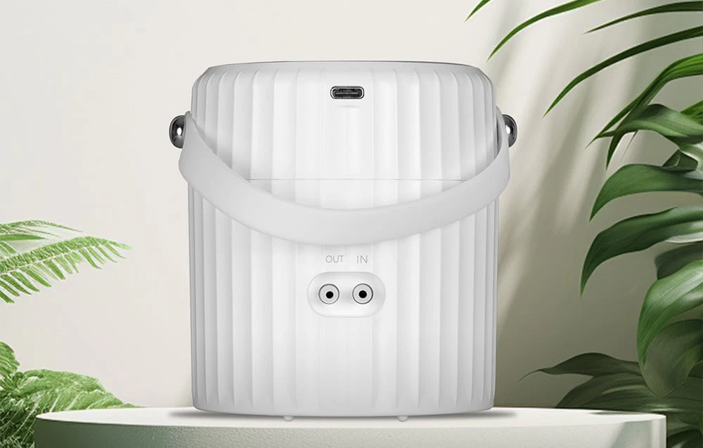 Dispozitiv alb, striat, cu mâner, port USB-C și intrări etichetate OUT și IN, pe fundalul unor plante