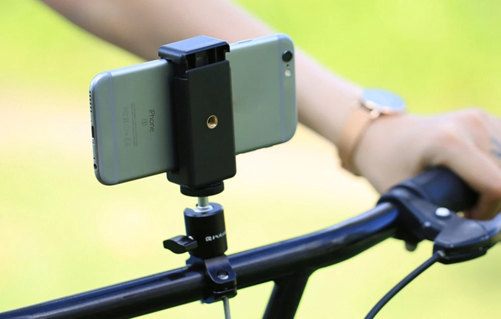 Un smartphone montat într-un suport atașat la ghidonul unei biciclete, ținut de o persoană pe un fundal verde estompat.