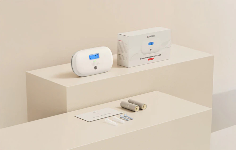 Detector de monoxid de carbon X-Sense cu afișaj LCD pe platformă, alături de ambalaj, baterii, instrucțiuni și accesorii de montare