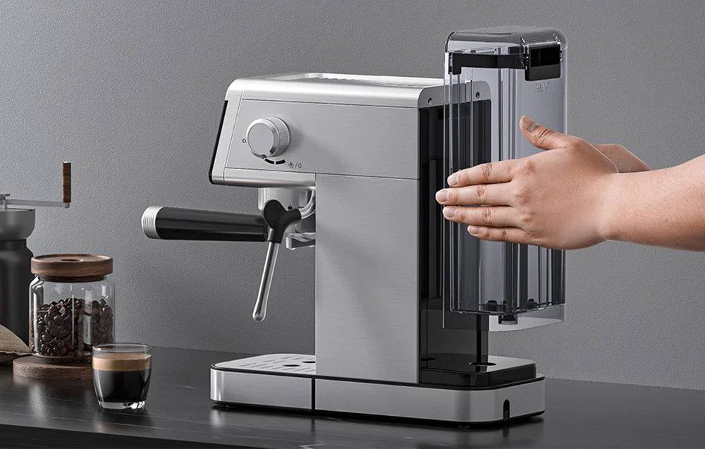 O mână instalează un rezervor de apă transparent într-o mașină de espresso din oțel inoxidabil