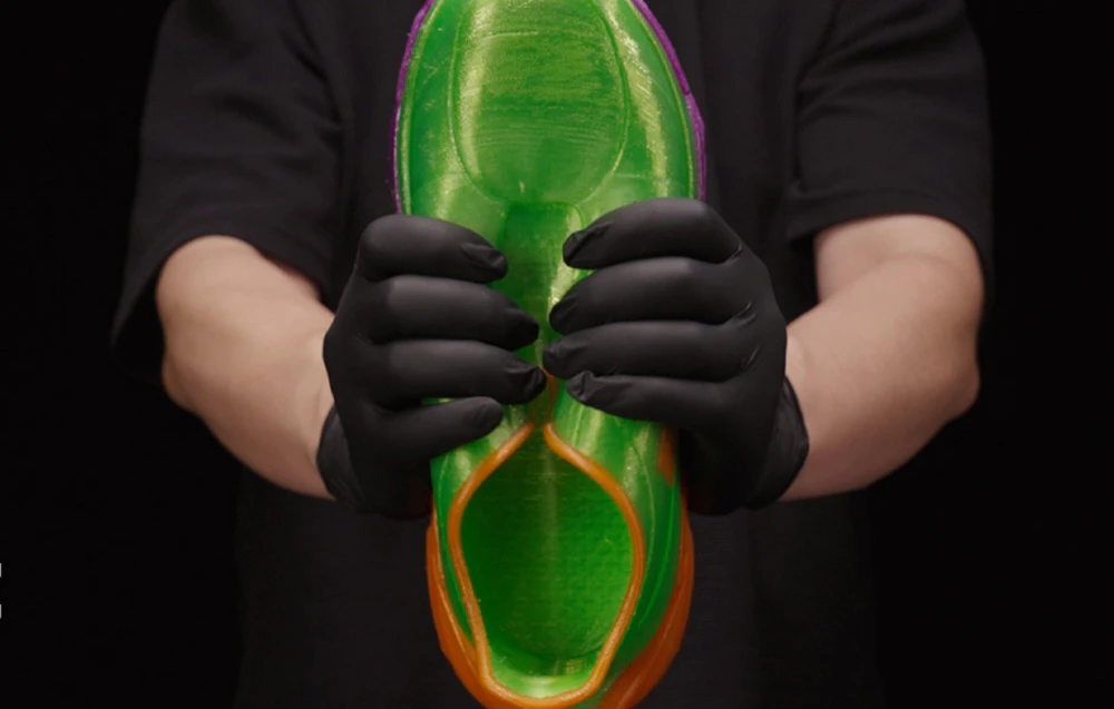 O talpă de pantof verde și violetă strânsă de mâini înmănușate