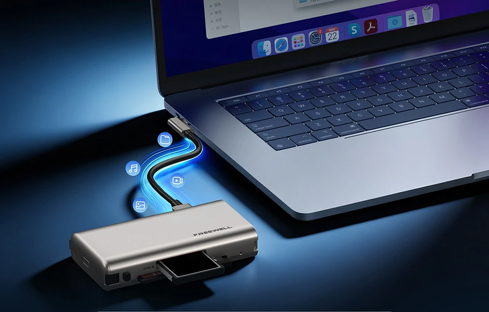 Un cititor de carduri Freewell argintiu cu carduri introduse, conectat printr-un cablu la un MacBook deschis, așezat pe o masă