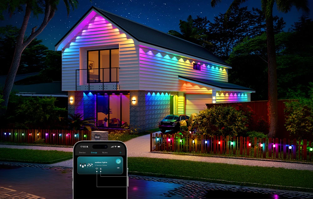 Casă iluminată de lumini colorate, cu un smartphone în prim-plan pe care rulează o aplicație de control al iluminatului
