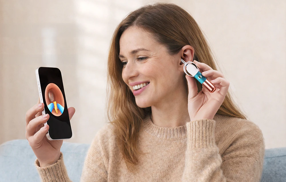 O femeie își curăță singură urechea folosind o pensetă integrată cu o cameră, în timp ce vizualizează imaginea pe ecranul smartphone-ului