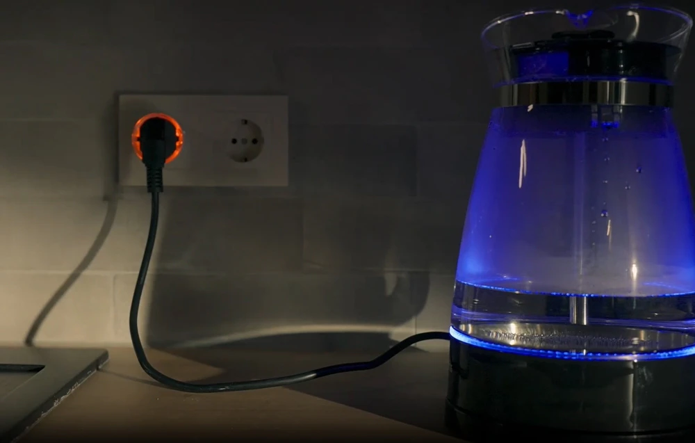 Ceainic electric conectat la o priză cu fișa Shelly Plug S iluminată în roșu