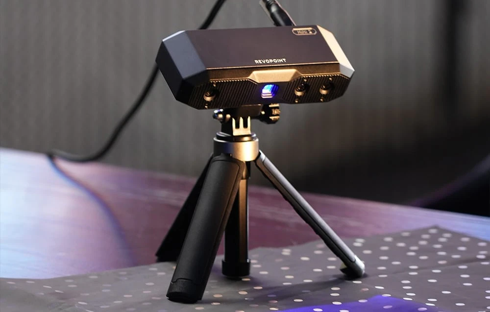 Scanerul 3D Revopoint Mini 2 cu lumina structurată albastră aprinsă, așezat pe un covoraș de calibrare