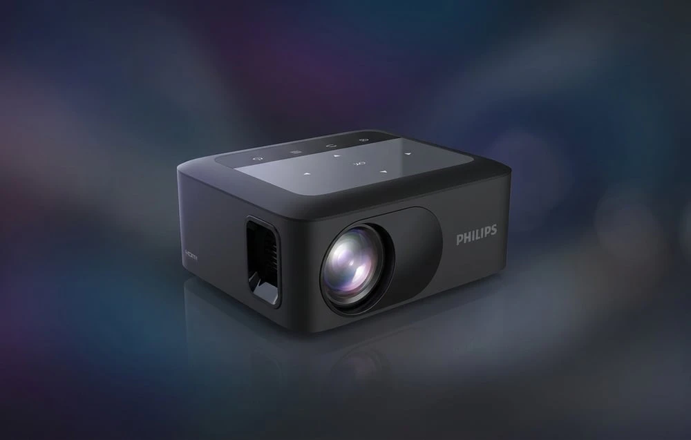 Un proiector PHILIPS negru cu inscripția „HDMI” pe lateral, așezat pe un fundal întunecat și estompat, cu puncte de lumină