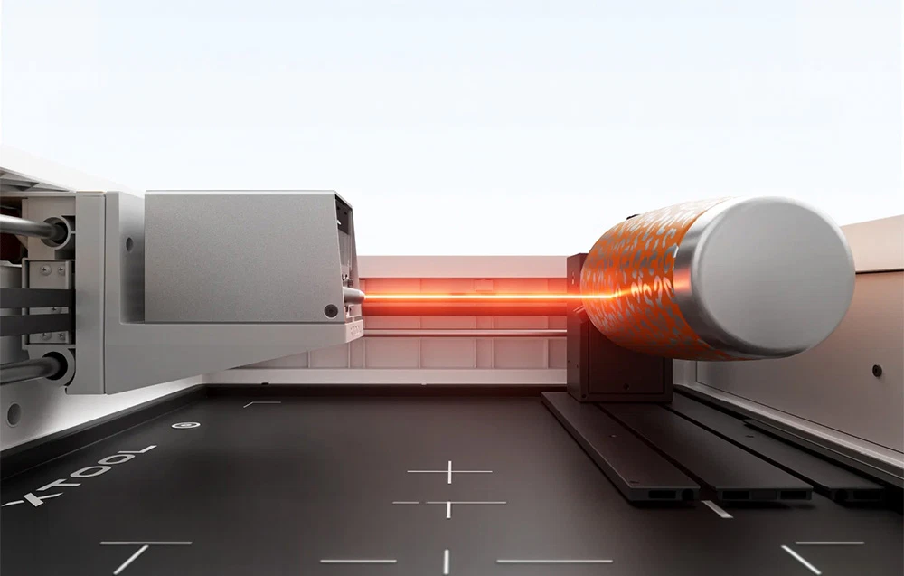 Interiorul plotterului xTool în timpul gravării cu laser pe o cană termică portocalie rotativă, cu un model