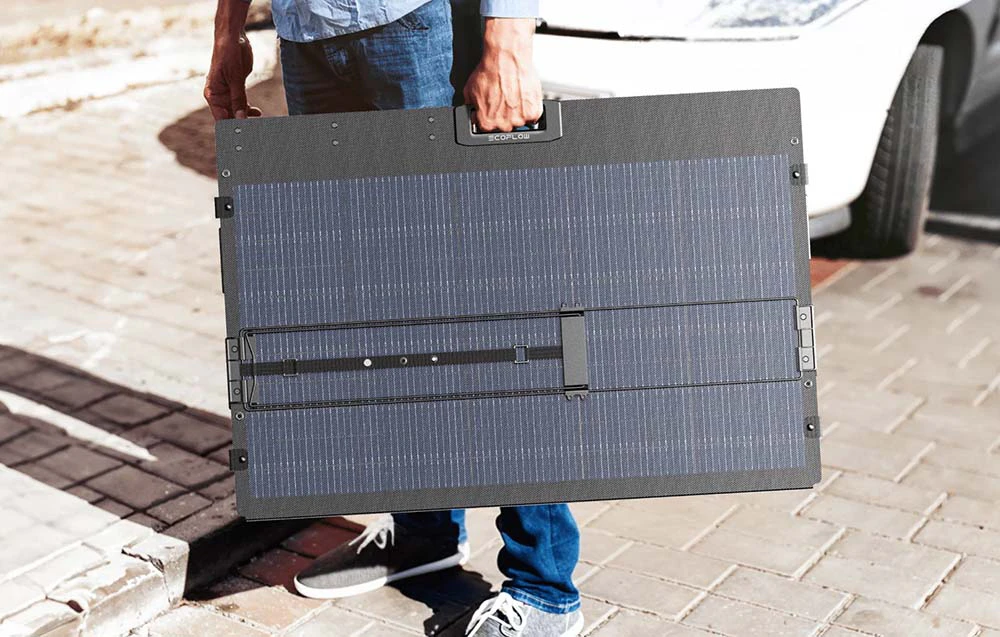 O persoană ținând un panou fotovoltaic portabil pliat, cu un mâner în centru