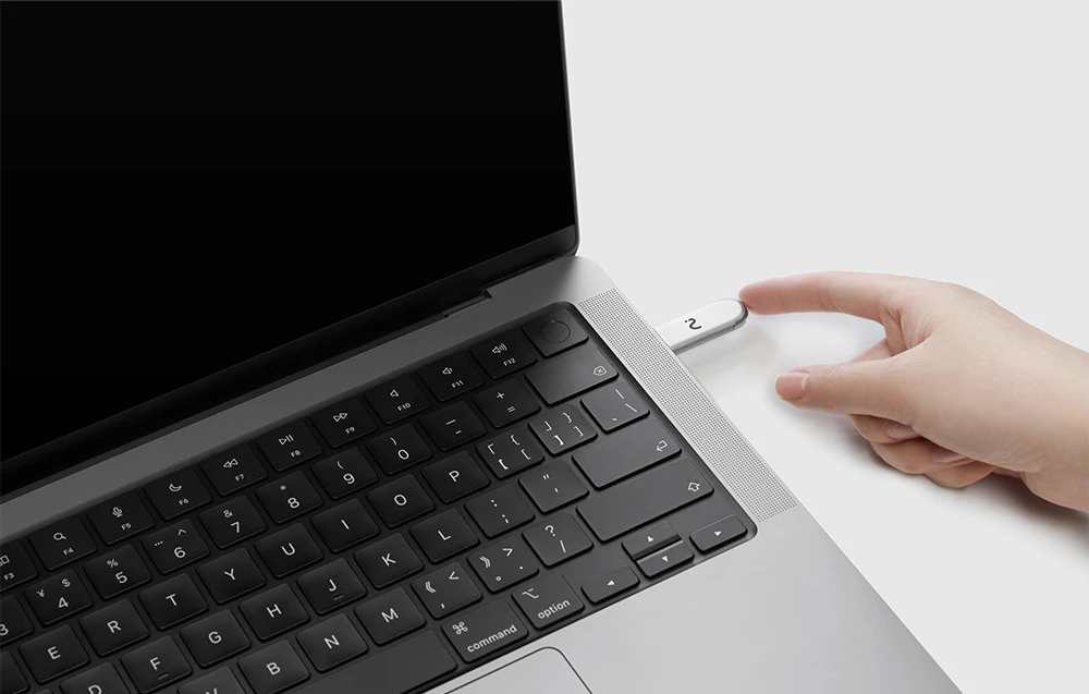 Un deget atinge dongle-ul metalic cu un LED verde, conectat la partea laterală a unui laptop deschis.