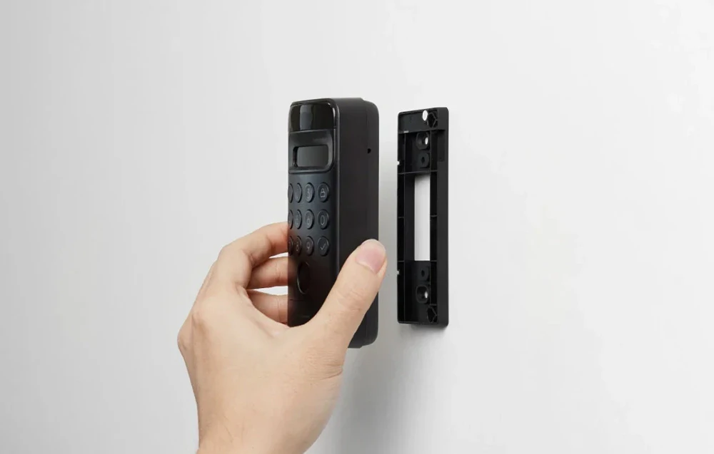 O mână care montează o tastatură numerică SwitchBot neagră pe un suport de montare pe perete