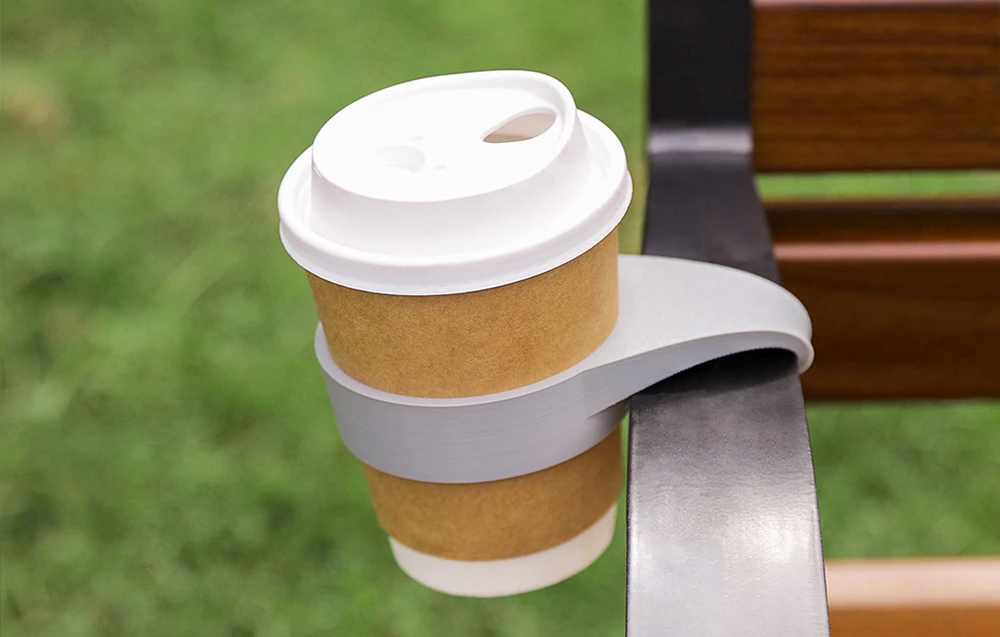 Cană de cafea cu capac și mâner gri fixat pe o balustradă metalică