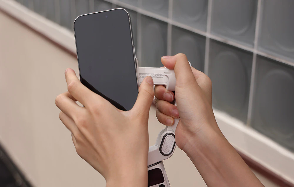 Mâini care atașează un smartphone la un suport magnetic pe un gimbal.