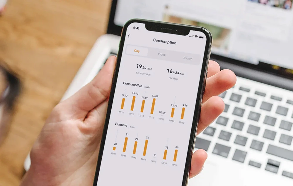 O mână care ține un smartphone cu aplicația Consumation afișând grafice ale consumului de energie electrică și ale timpului de funcționare