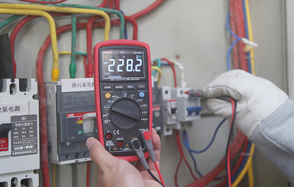 Măsurarea tensiunii într-un aparat de comutație electrică folosind un multimetru digital și o sondă ținută într-o mănușă temporară.