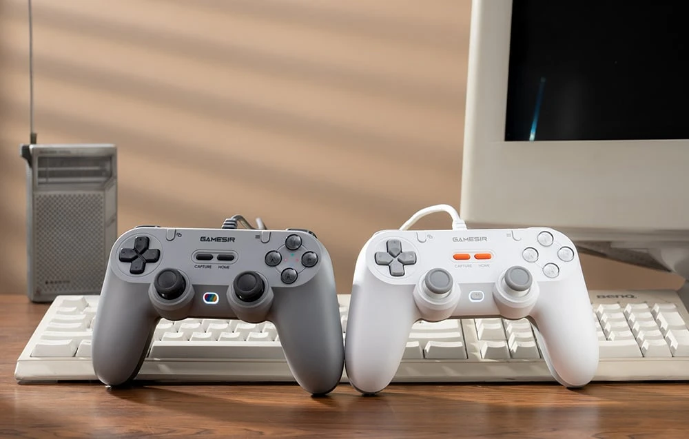 Controler GameSir gri și alb așezat pe tastatură în fața monitorului și a radioului.