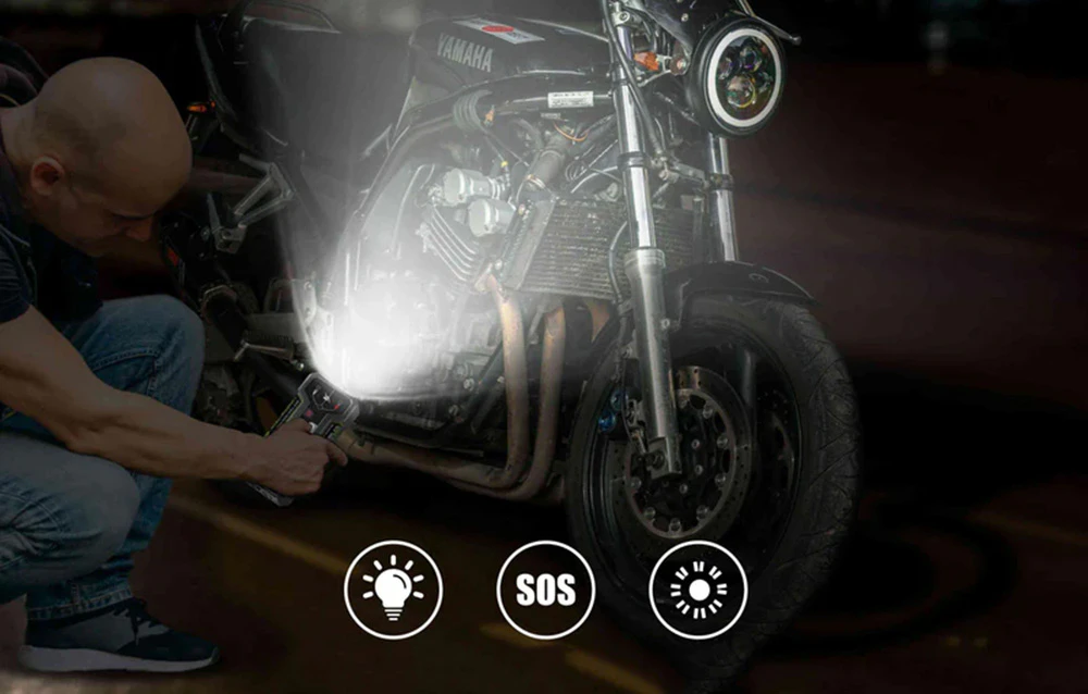 Un bărbat luminează cu lanterna încorporată în dispozitivul de pornire LOKITHOR motorul unei motociclete.