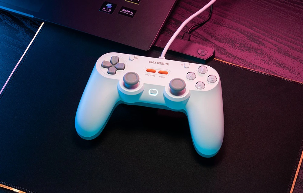 Controler GameSir alb cu cablu conectat la un laptop și așezat pe un pad.