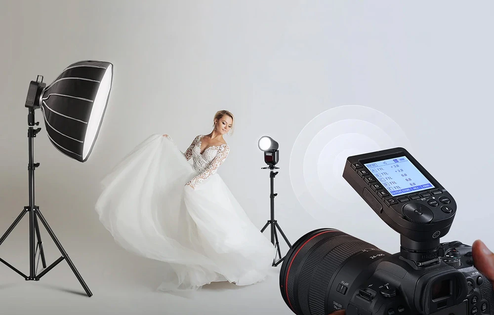 O femeie în rochie de mireasă pozează într-un studio foto lângă blițuri și un aparat foto cu transmițător.