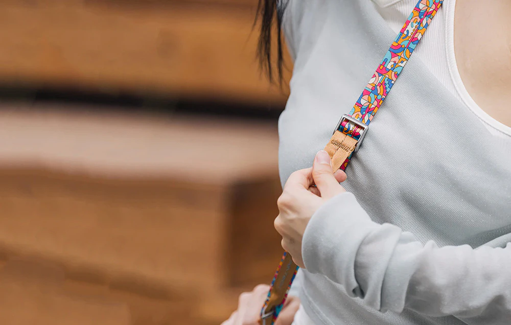 O femeie într-un tricou deschis la culoare ajustează lungimea curelei PGYTECH, care este atârnată pe umăr