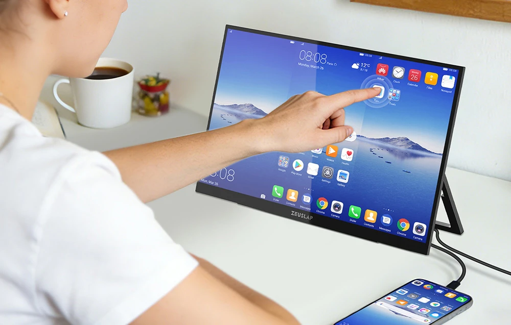 O persoană atinge ecranul tactil al unui monitor ZEUSLAP conectat la un smartphone aflat pe un birou