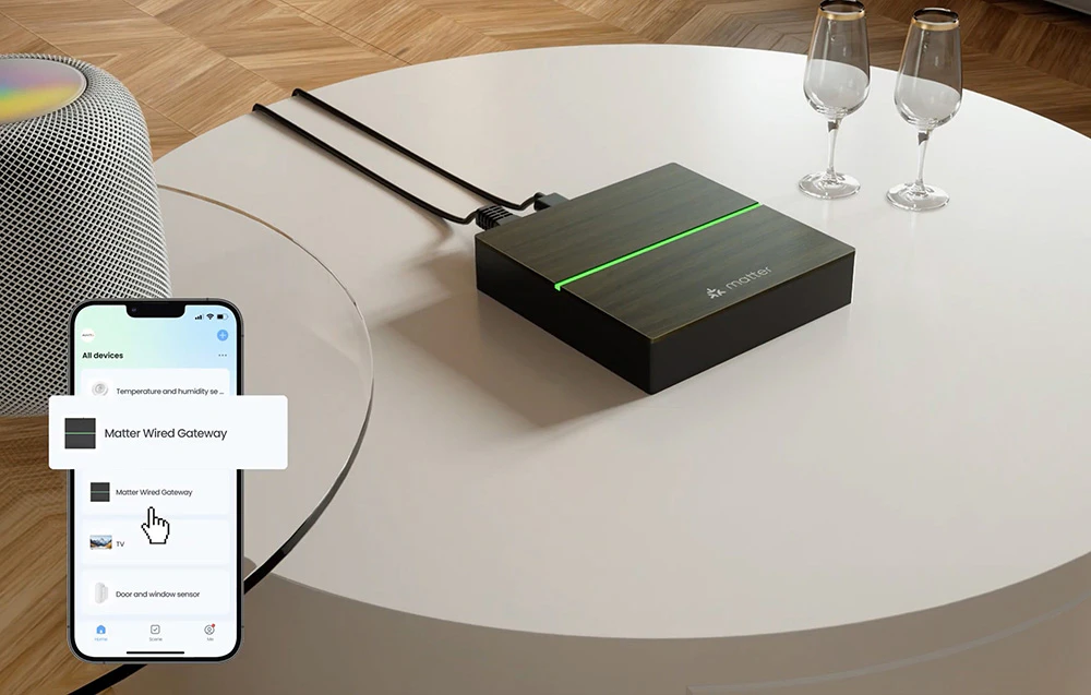 Dispozitivul Matter pe masa rotundă cu cablurile conectate vizibile, cei doi ochelari și smartphone-ul care prezintă interfața aplicației cu dispozitivul Matter Wired Gateway detectat