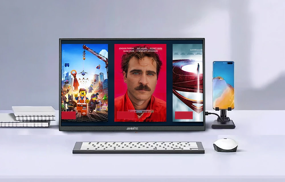 Ecranul portabil așezat pe un birou afișează afișe de filme lângă o tastatură, un mouse și un telefon.