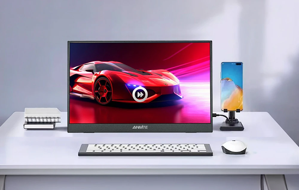 Un monitor de birou pe care se vede o mașină roșie, cu o tastatură, un mouse și un telefon așezate pe un suport lângă el.
