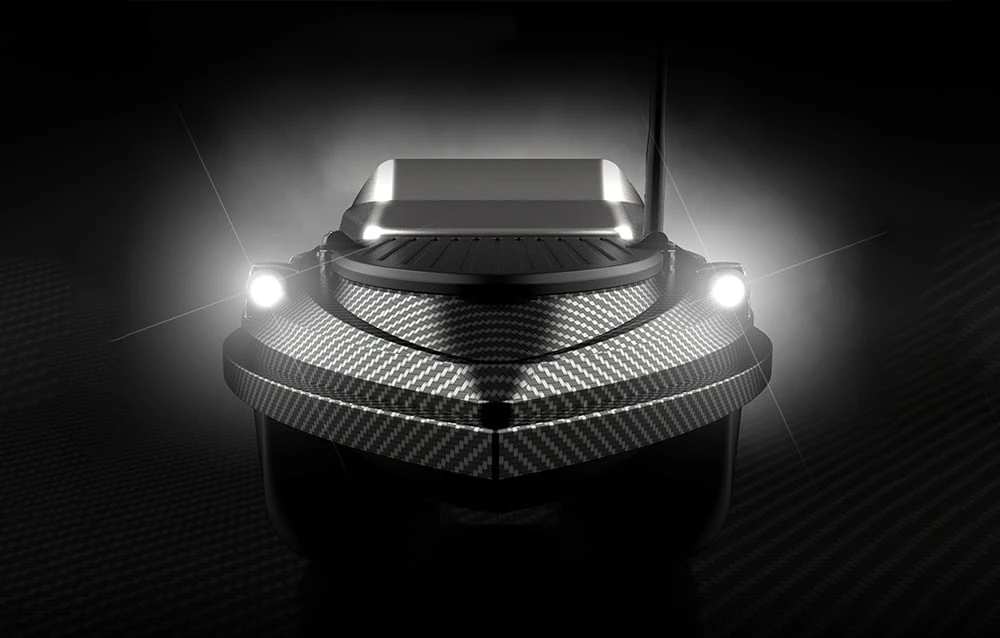 Vedere frontală a unei bărci de momeală RC din carbon cu două spoturi albe puternice și o lumină LED pe un fundal negru