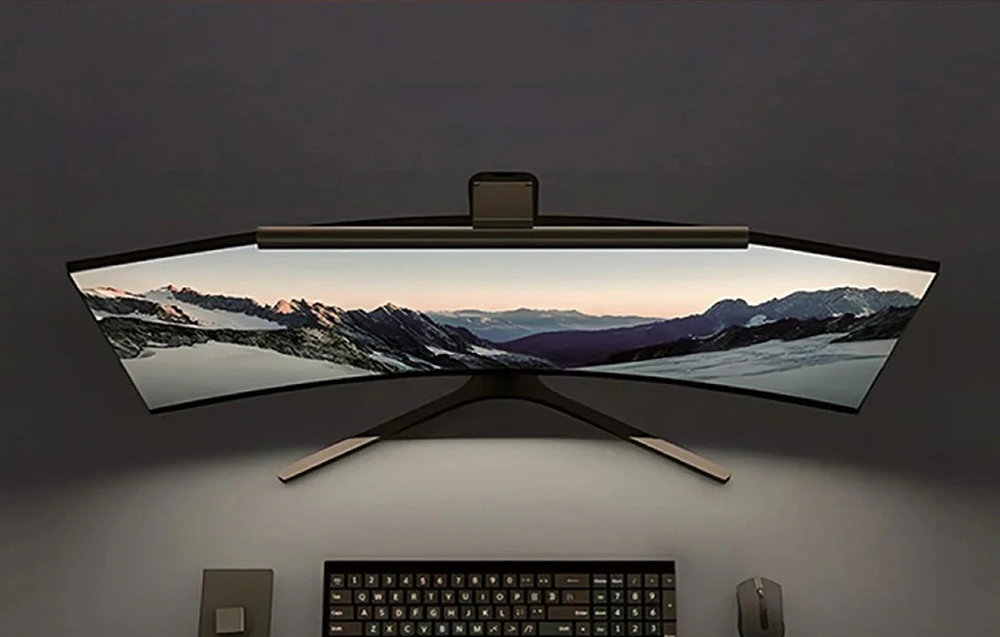 Vedere de sus a unui monitor curbat cu o lampă Yeelight montată; în fața acestuia se află o tastatură și un mouse