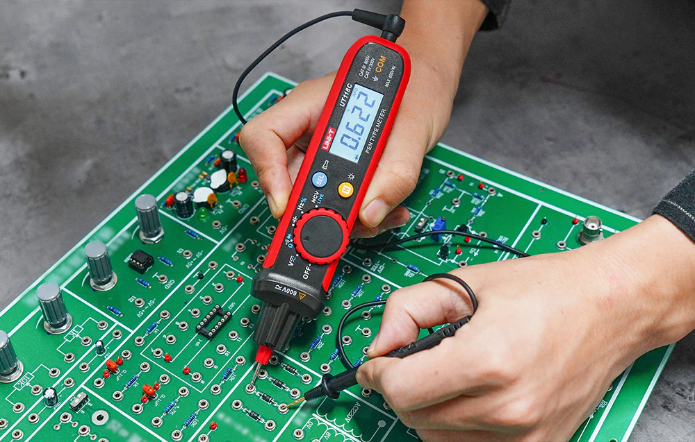 Testarea unei plăci de circuit imprimat (PCB) verzi folosind un multimetru digital portabil în formă de stilou.