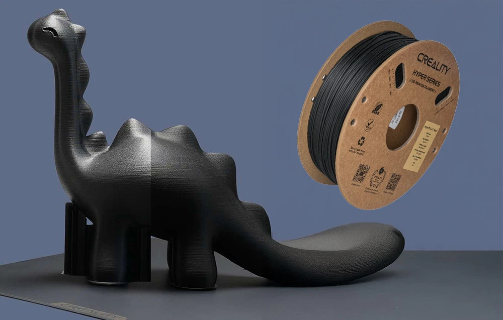 Un model negru de dinozaur imprimat pe o imprimantă 3D lângă o bobină de filament Creality Hyper Series
